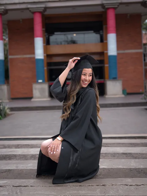 Graduada levantando su diploma frente a la facultad