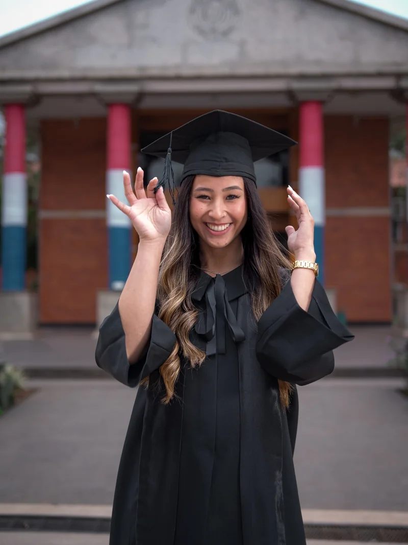Graduada sonriente con toga frente a su facultad